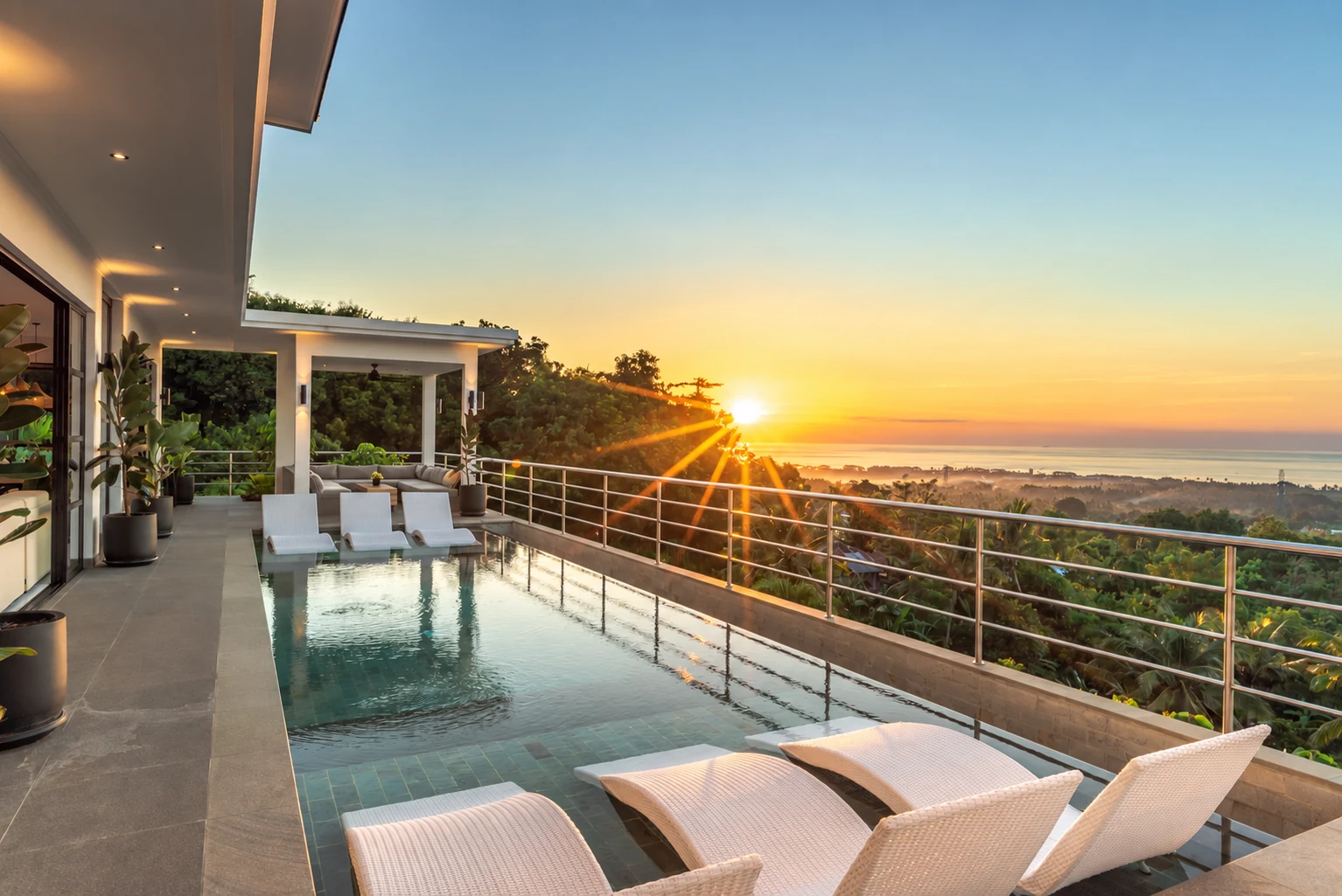 Upper pool at golden hour, sun over ocean, white loungers, shaded gazebo.