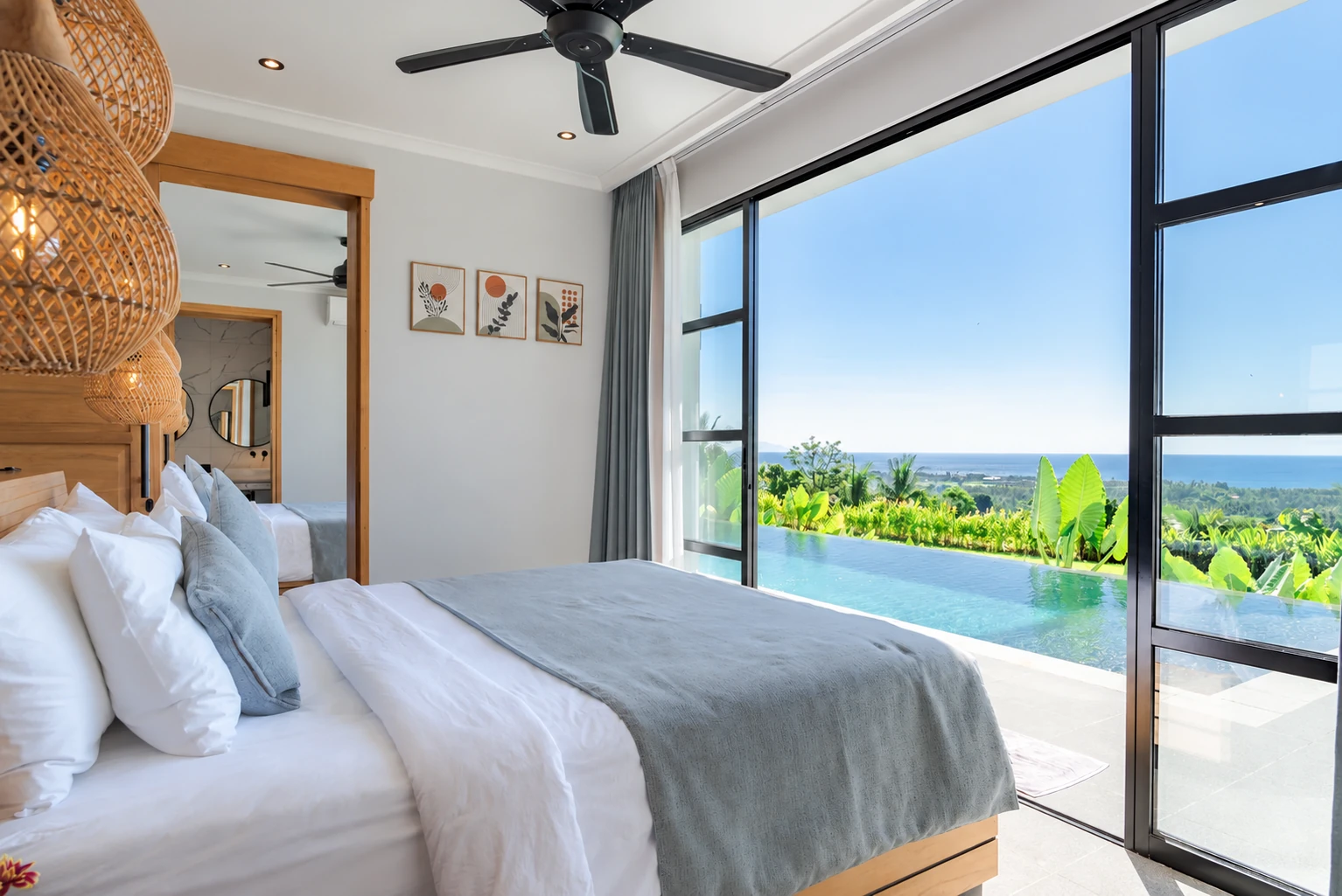 Bedroom with white linen, woven pendants and sliding doors toward lower pool and sea.