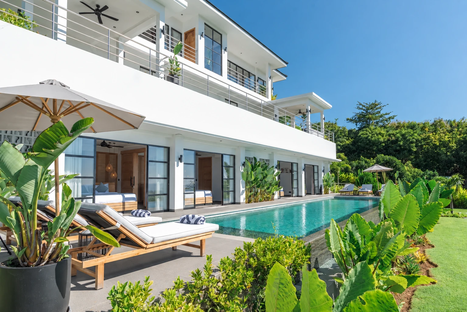 Lower pool beside row of bedroom doors, lounger terrace and greenery.