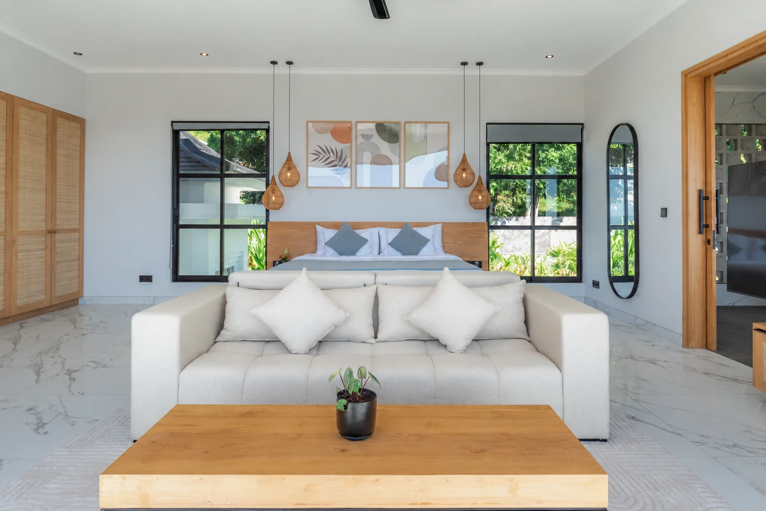 Spacious master suite with bed, timber headboard, sitting area and light stone floor.
