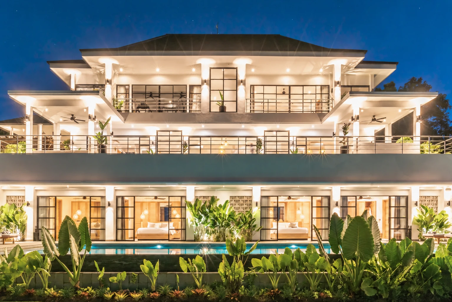 Front elevation illuminated at blue hour; warm interior light against deep blue sky.